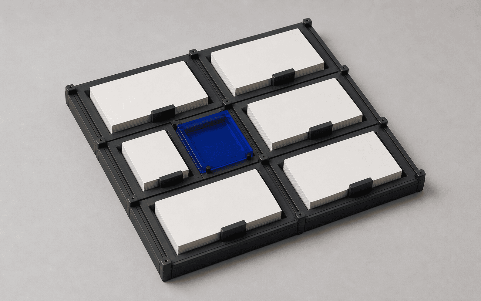 A modular graphite tray of ivory paper stacks with one cobalt acrylic compartment